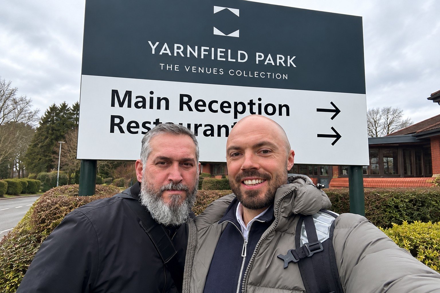 Two business colleagues standing together outside Yarnfield Park, with the venue sign in the background.