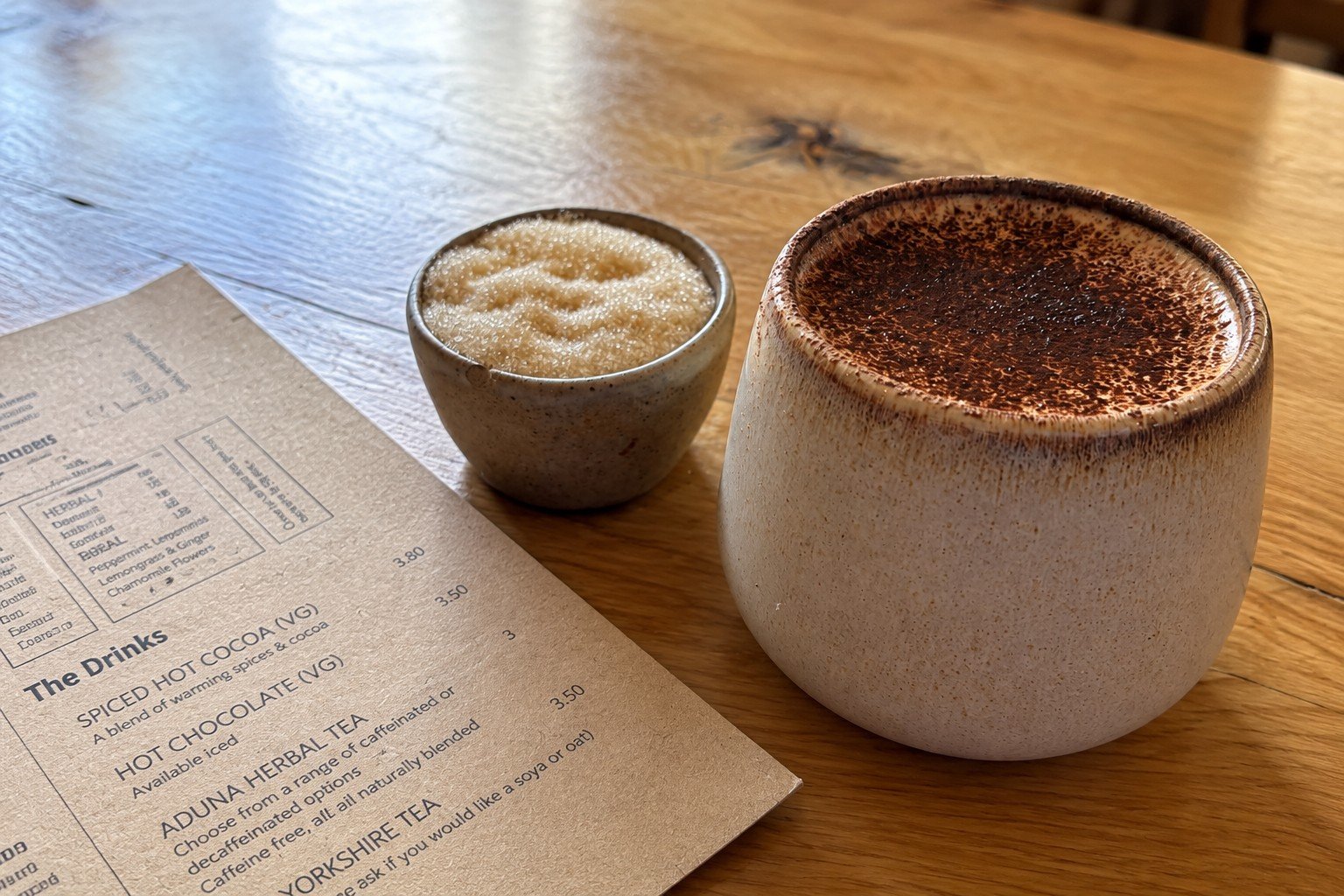 A warm drink in a ceramic cup on a wooden café table, alongside a drinks menu.